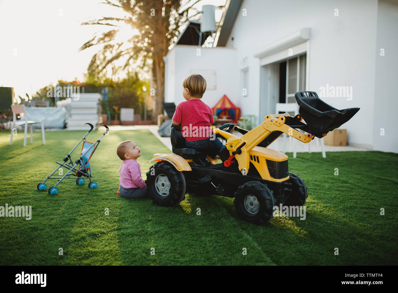 Una bambina e un bambino seduto su un trattore giocattolo in cantiere Foto Stock