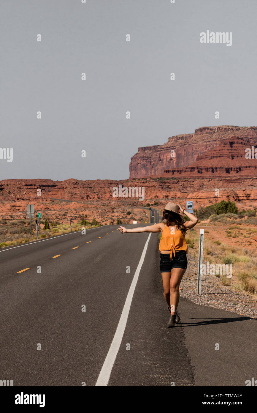 Donna autostop mentre si cammina sulla strada contro il cielo chiaro alla Monument Valley Tribal Park durante la giornata di sole Foto Stock