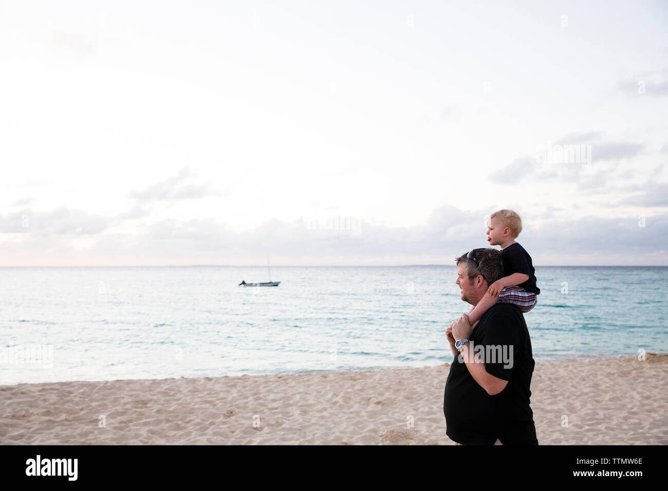 Felice padre figlio che porta sulle spalle mentre si sta in piedi in spiaggia Foto Stock