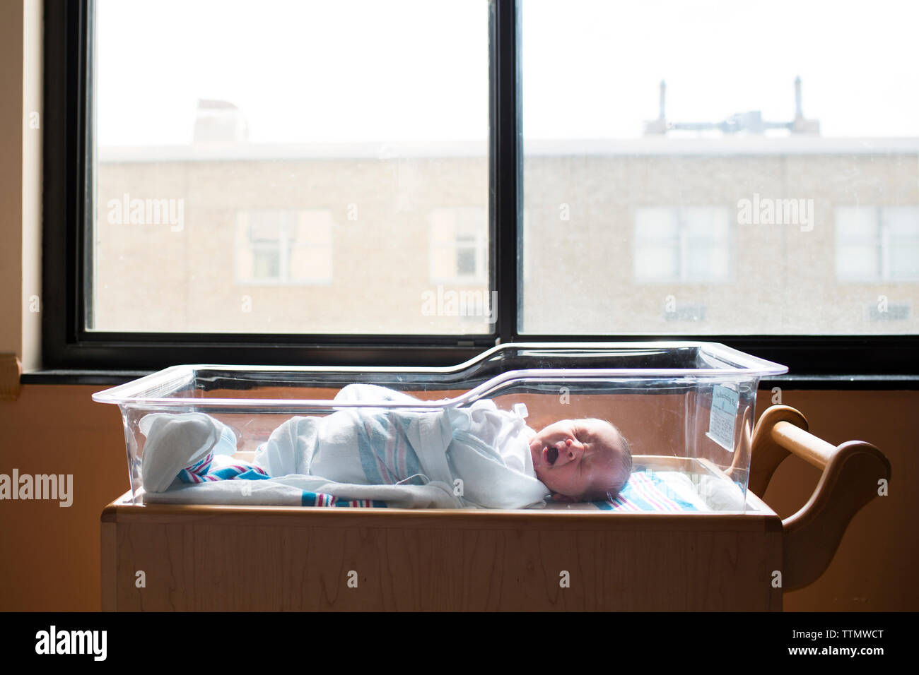 Baby boy sbadigliare mentre dormono in culla dalla finestra in ospedale Foto Stock