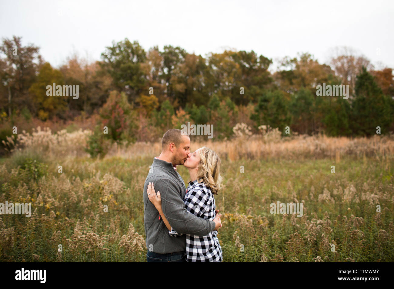 Vista laterale della coppia romantica baciare stando in piedi in mezzo a piante contro il cielo chiaro nella foresta Foto Stock