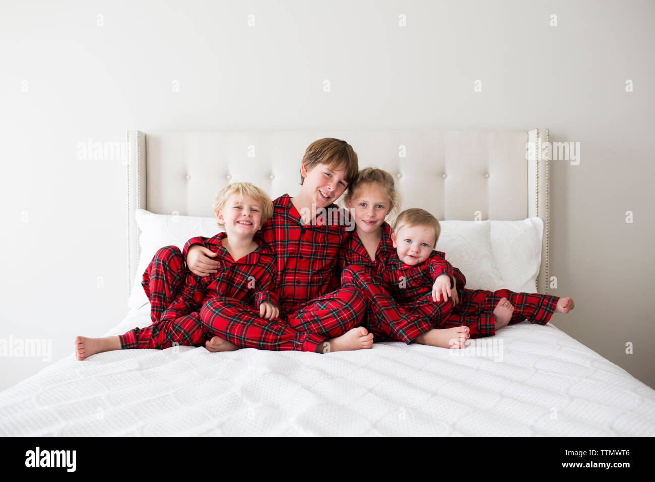 Quattro fratelli sorridente indossando pigiami di Tartan pongono abbracciando sul letto bianco Foto Stock