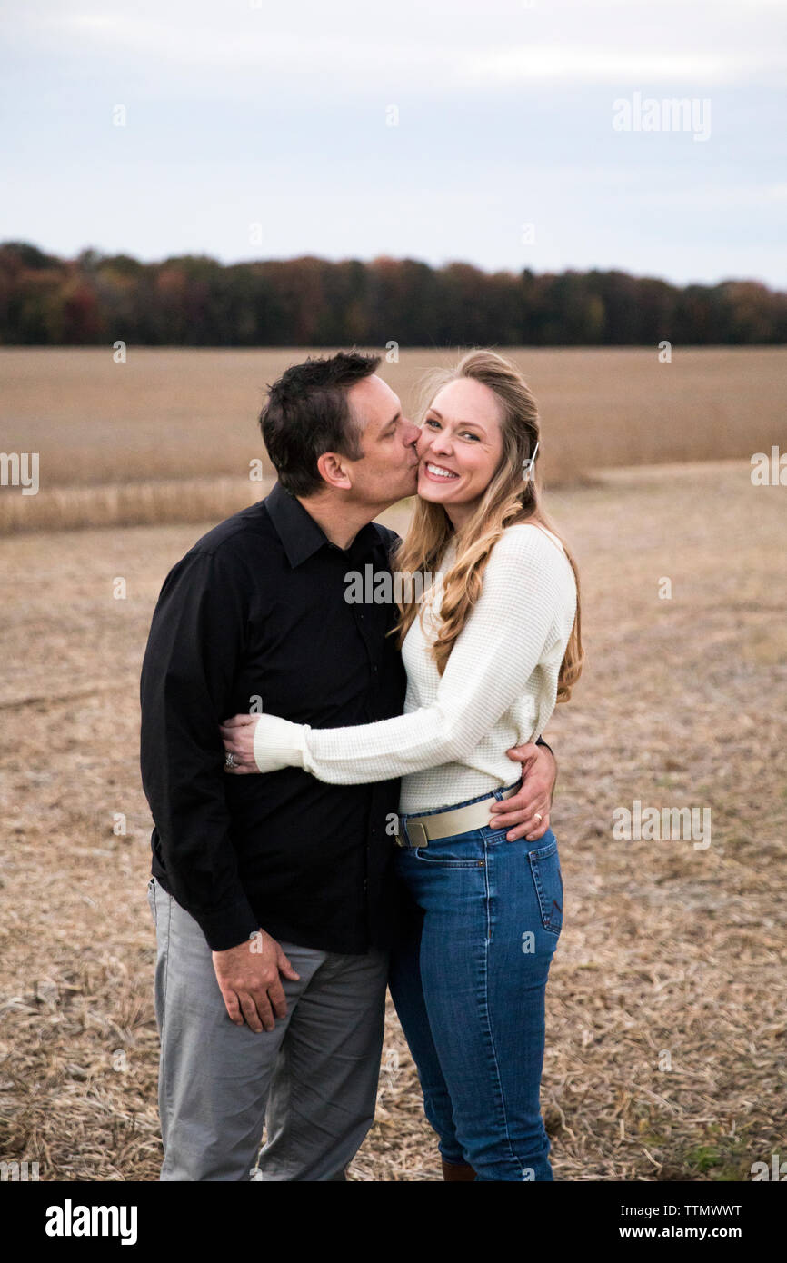 Papà baci sorridente Mom sulla guancia, in piedi nel campo di fattoria al tramonto Foto Stock