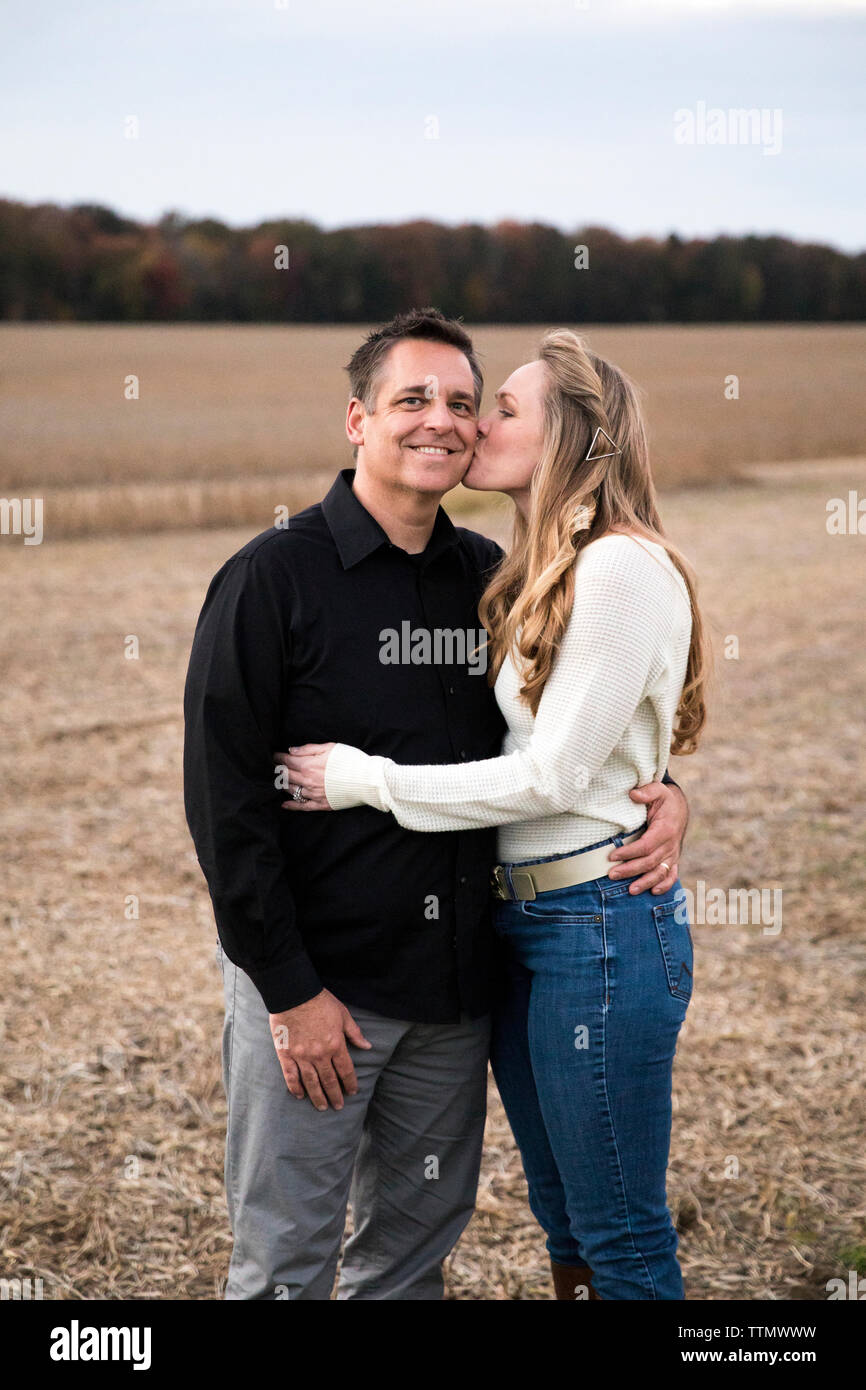 Mom baci sorridente papà sulla guancia, in piedi nel campo di fattoria al tramonto Foto Stock