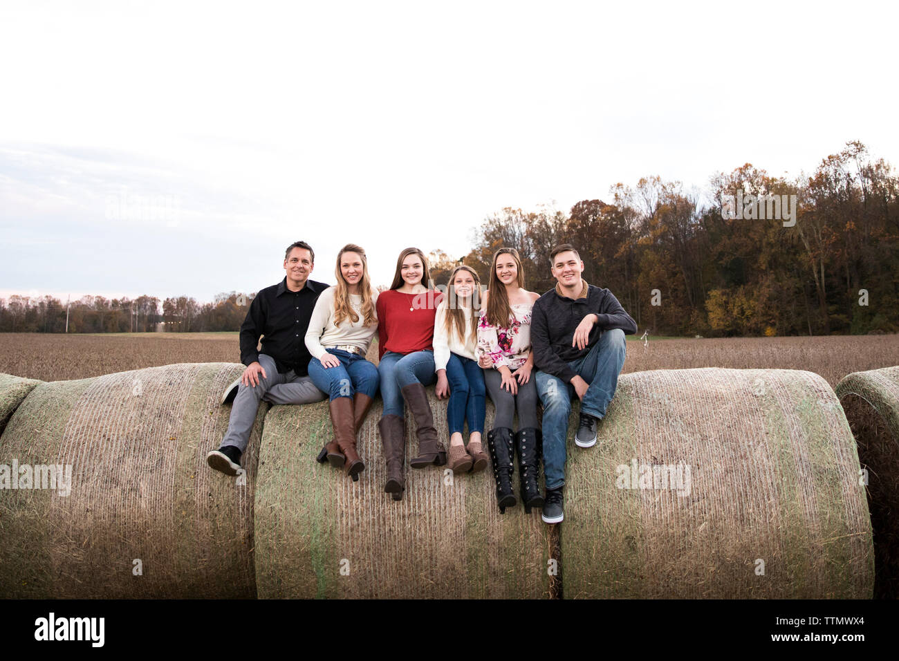 Ampia vista della grande famiglia felice seduti su balle di fieno nel campo al tramonto Foto Stock