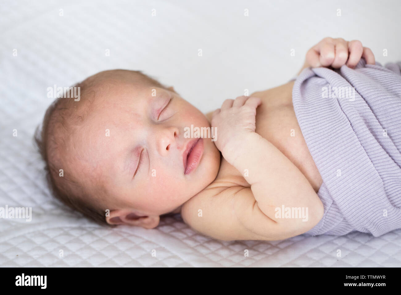 Sleeping Neonato ragazza in viola un lenzuolo sul letto bianco Foto Stock