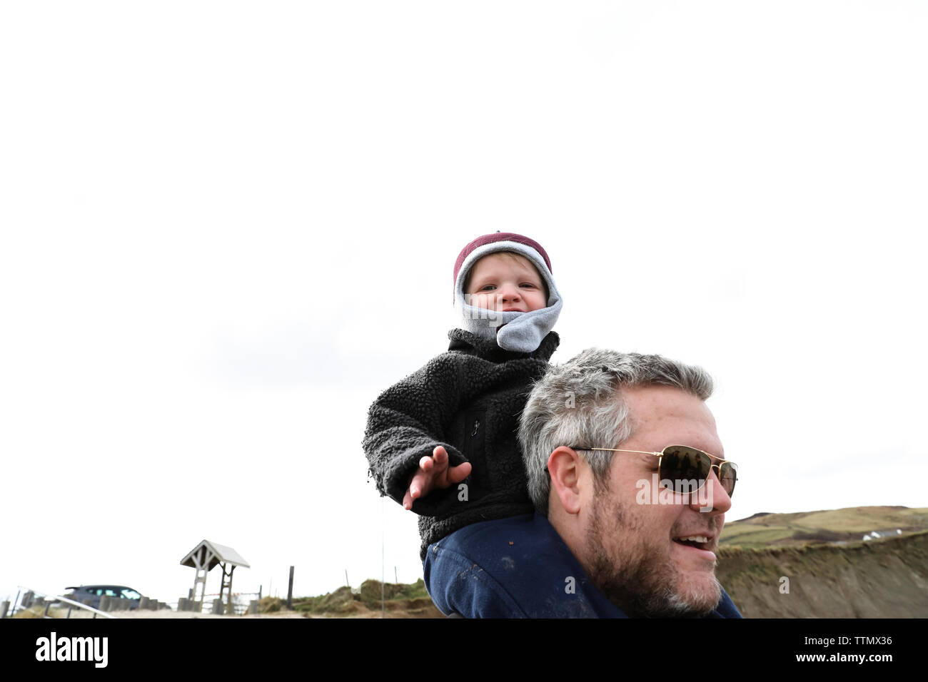 Bassa vista del bambino seduto sul suo papà spalle sulla spiaggia irlandese Foto Stock