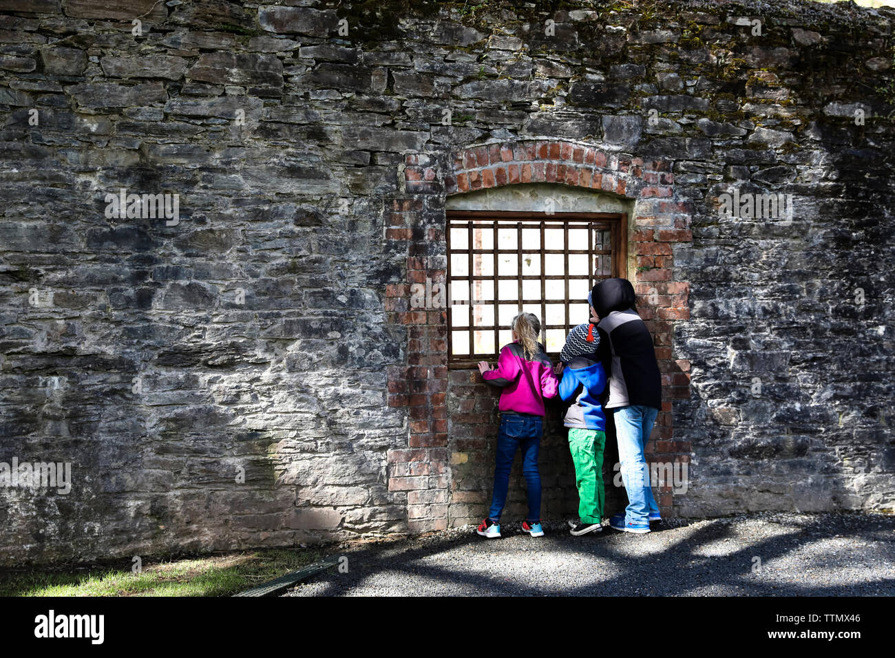 Tween Boy e Fratelli Minori guardare attraverso la finestra di ferro nel muro di pietra Foto Stock