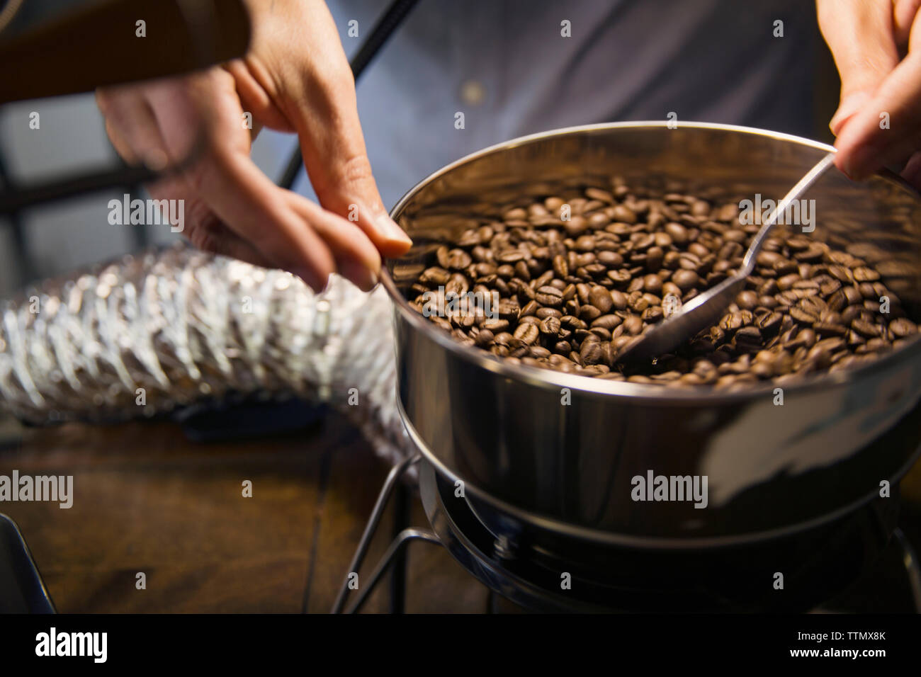 Sezione mediana dell'uomo la tostatura i chicchi di caffè in macchinari presso il cafe Foto Stock