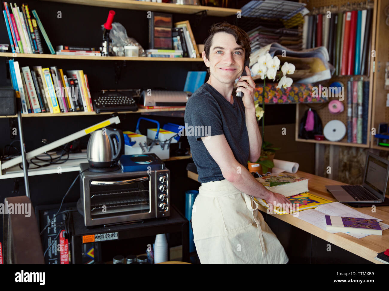 Vista laterale ritratto di sorridente giovane uomo utilizzando un telefono cordless in piedi presso l'ufficio domestico Foto Stock