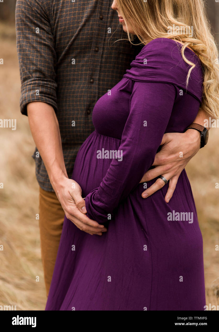 Sezione mediana del marito abbracciando moglie incinta mentre sta in piedi all'aperto Foto Stock