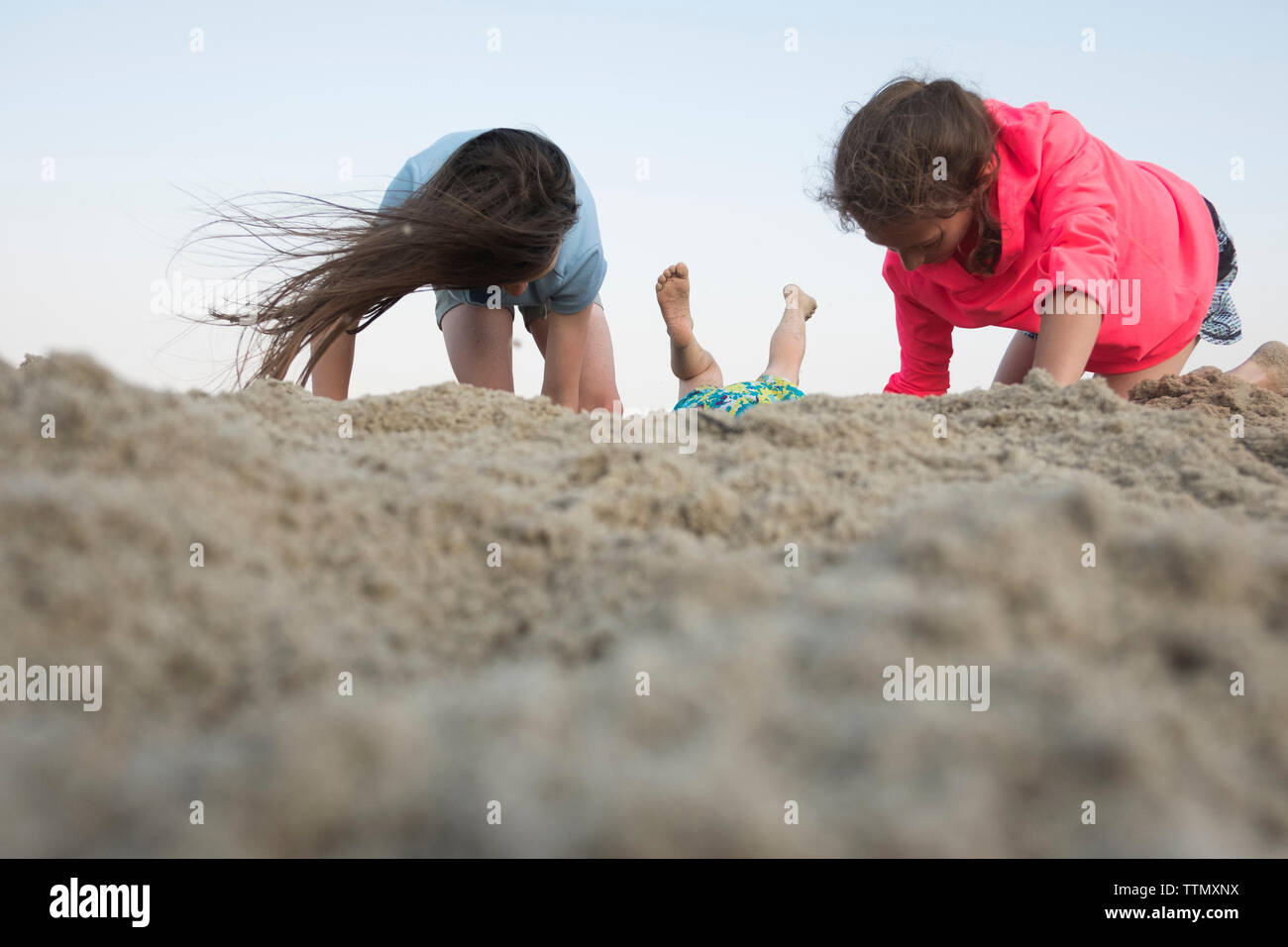 Superficie di livello immagine delle sorelle il gioco con la sabbia in spiaggia contro il cielo chiaro Foto Stock