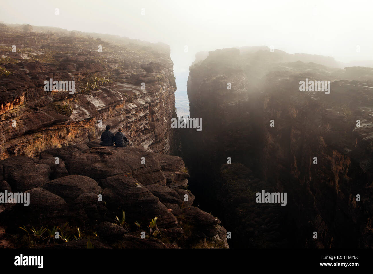 Vista posteriore di amici seduti sulla roccia nella nebbia meteo Foto Stock