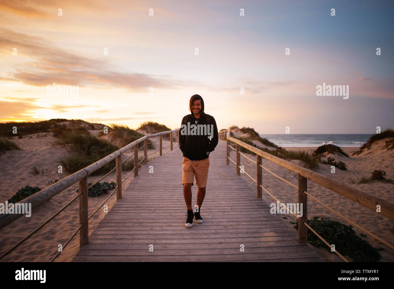 Sorridendo gli escursionisti a piedi su passerella in spiaggia contro il cielo durante il tramonto Foto Stock