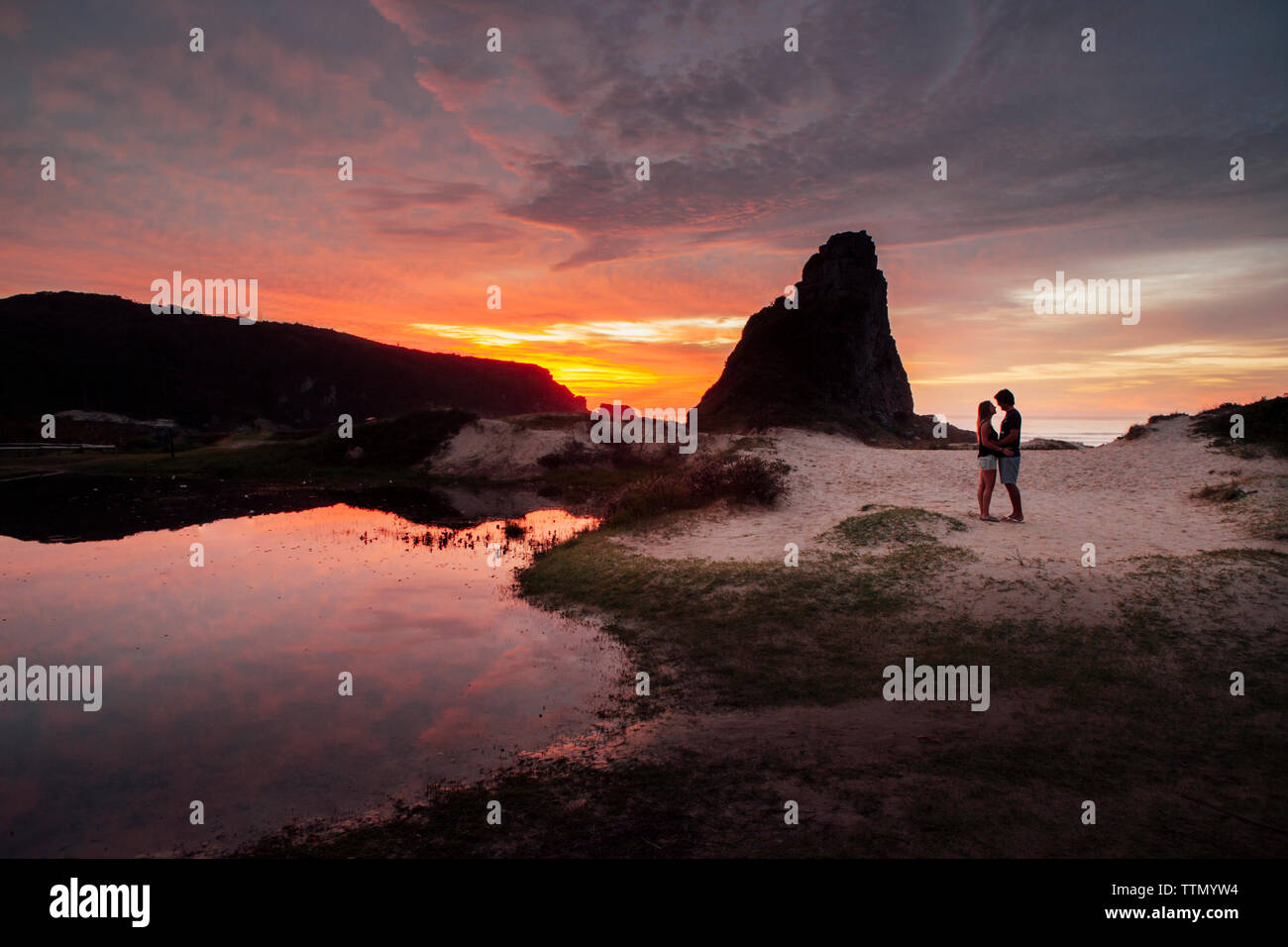 Coppia romantica permanente sulla sabbia contro il cielo durante il tramonto Foto Stock