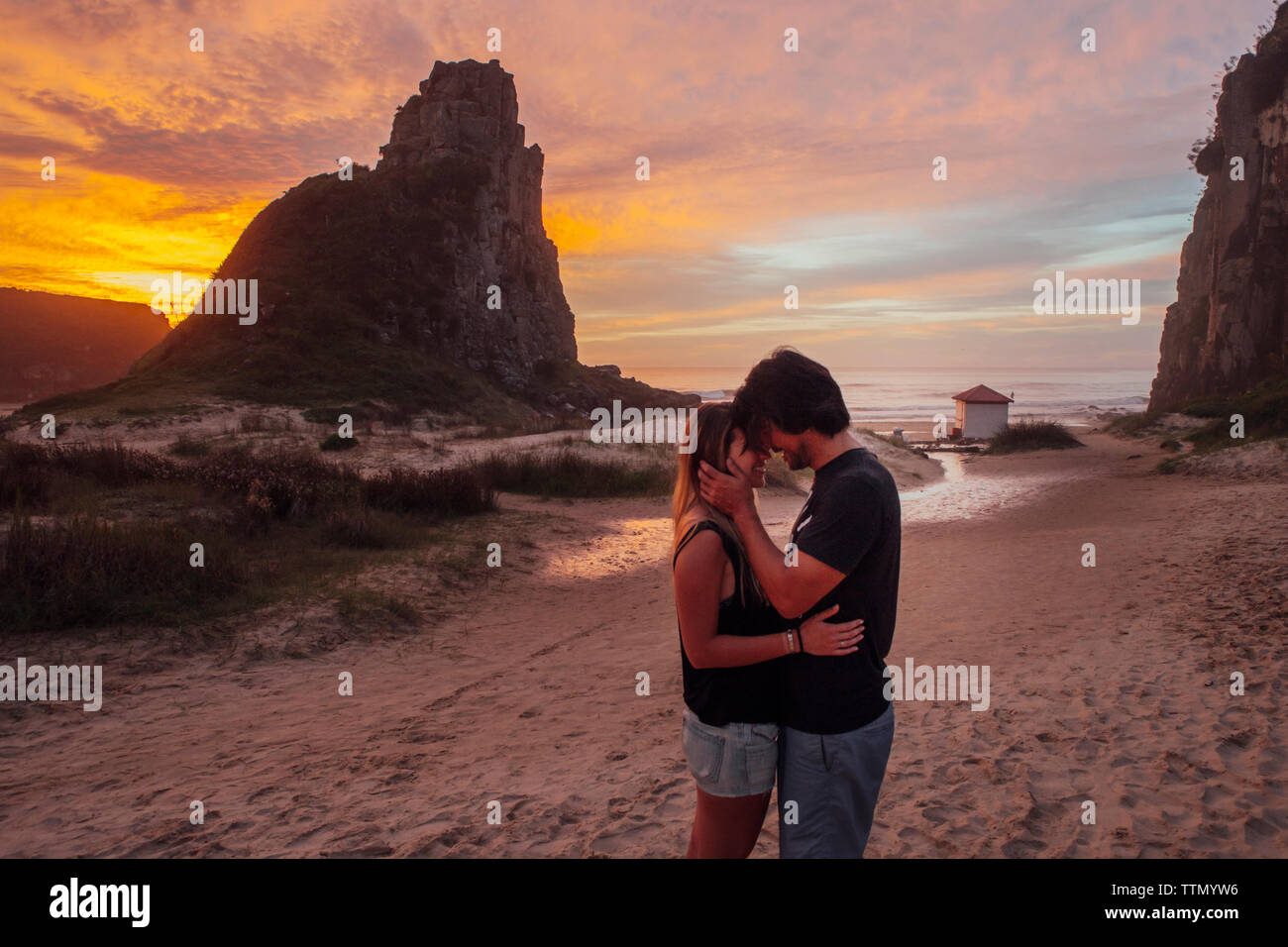 Vista laterale della coppia romantica in piedi in spiaggia durante il tramonto Foto Stock