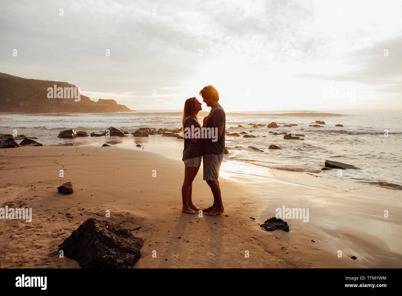 Vista laterale della coppia romantica in piedi faccia a faccia presso la spiaggia Foto Stock