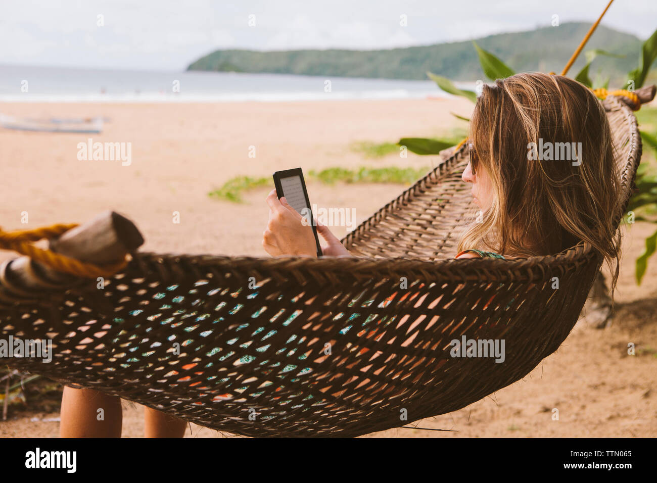 Donna che utilizza computer tavoletta mentre vi rilassate sulle amache in spiaggia Foto Stock