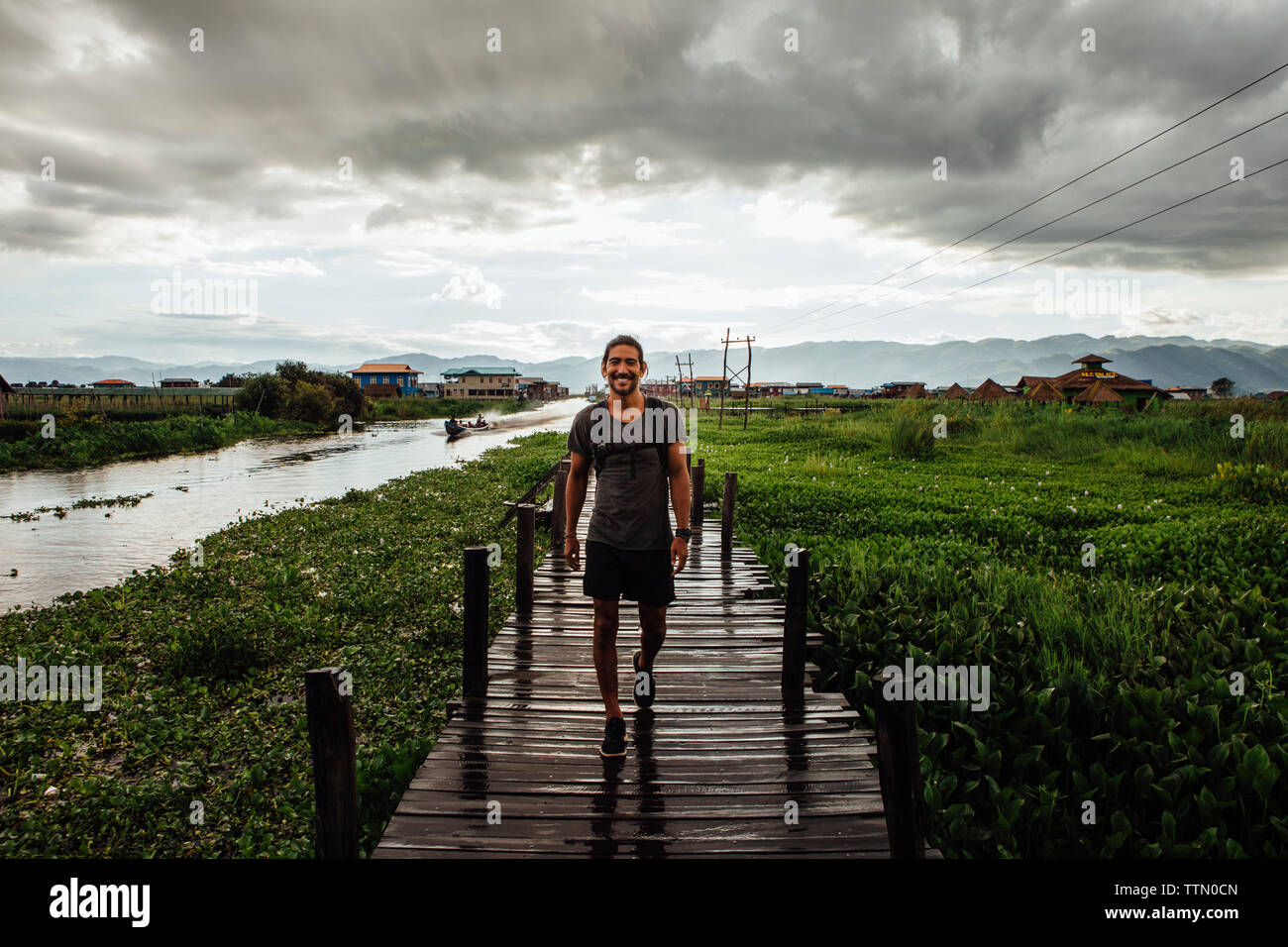 Ritratto di uomo che cammina sulla passerella dal Lago Inle contro il cielo nuvoloso Foto Stock