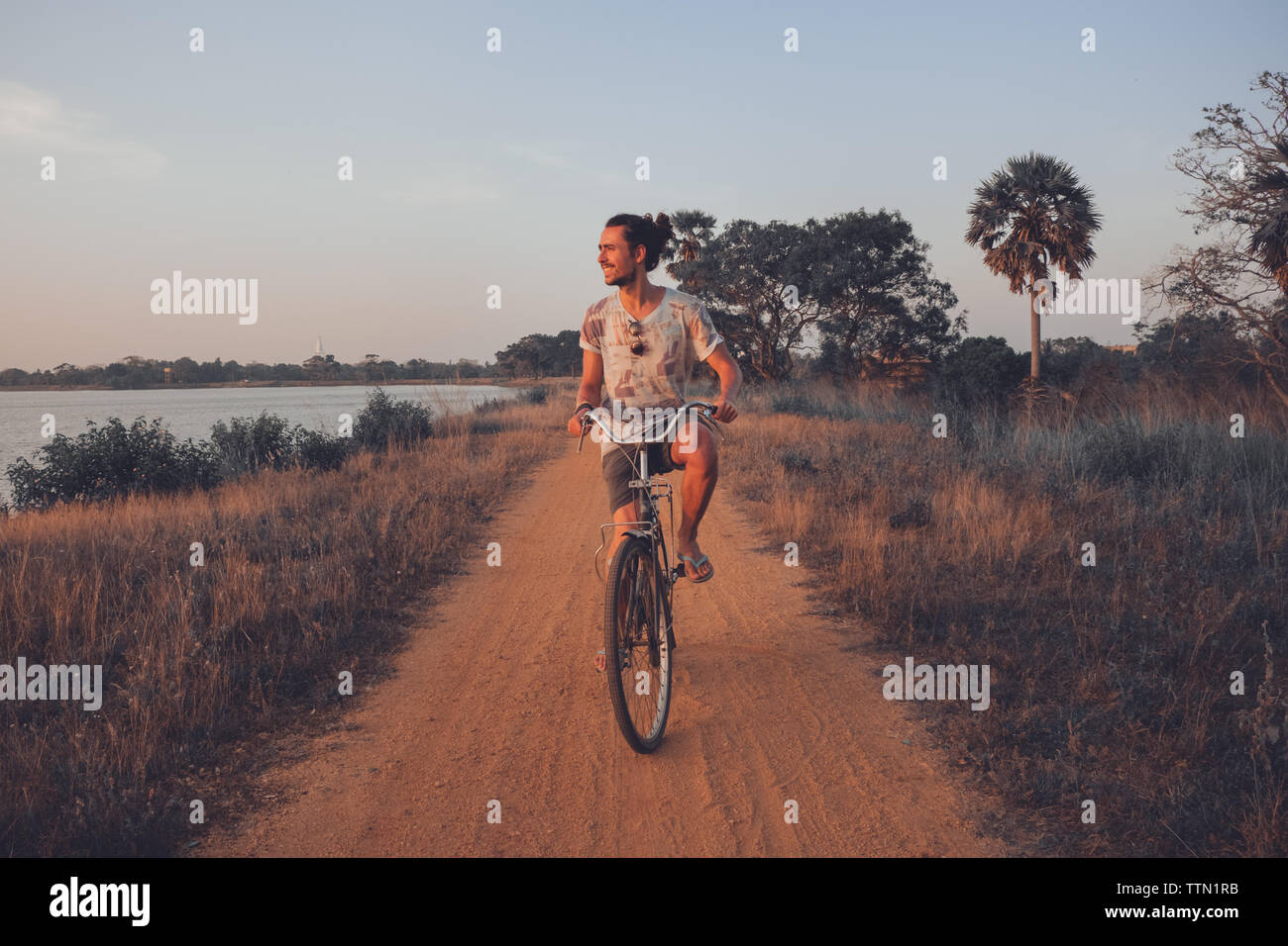 Uomo sorridente mentre in sella alla sua bicicletta all'aperto in estate Foto Stock