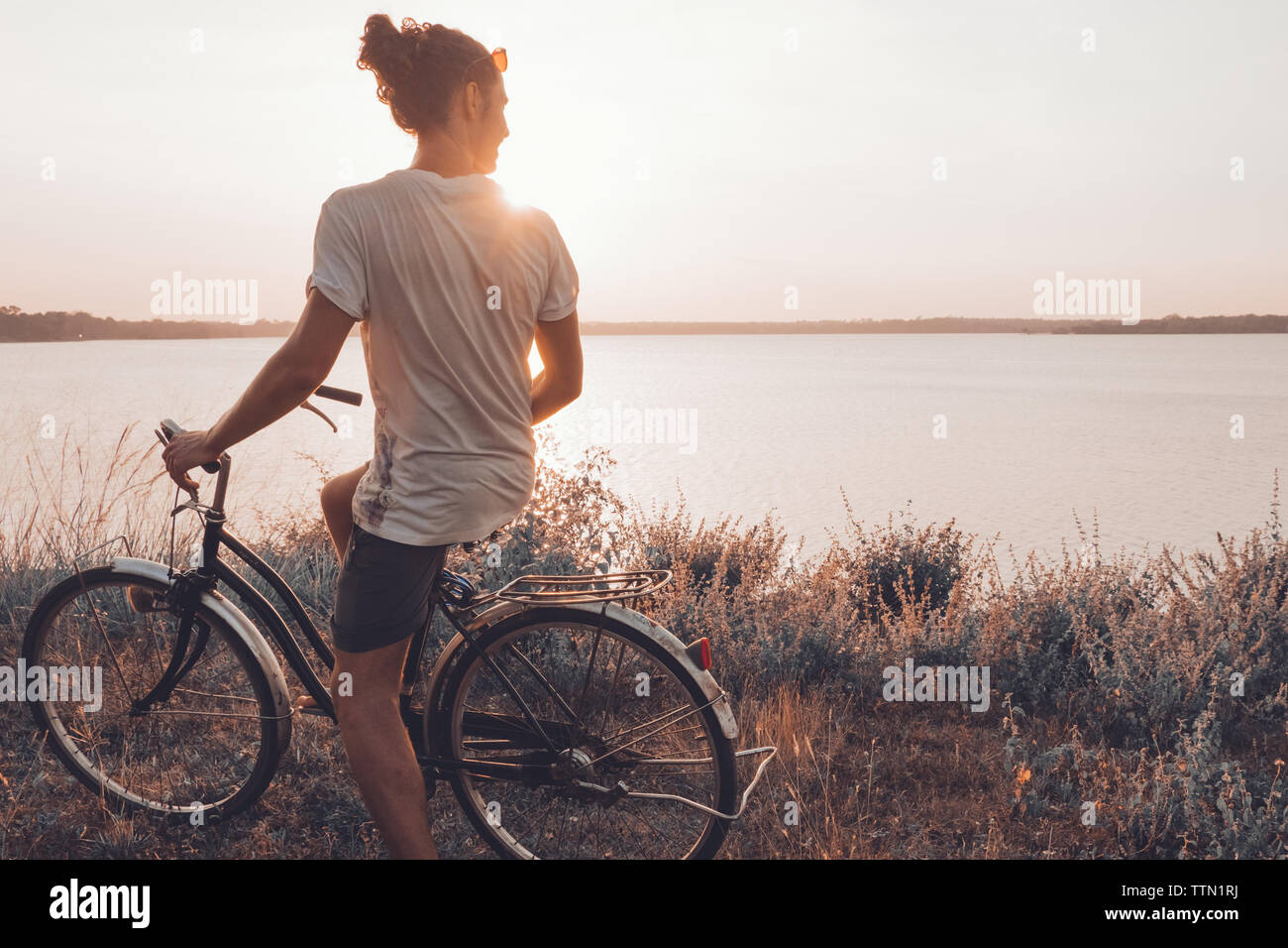 Uomo in piedi sulla sua bicicletta all'aperto in estate durante il tramonto Foto Stock