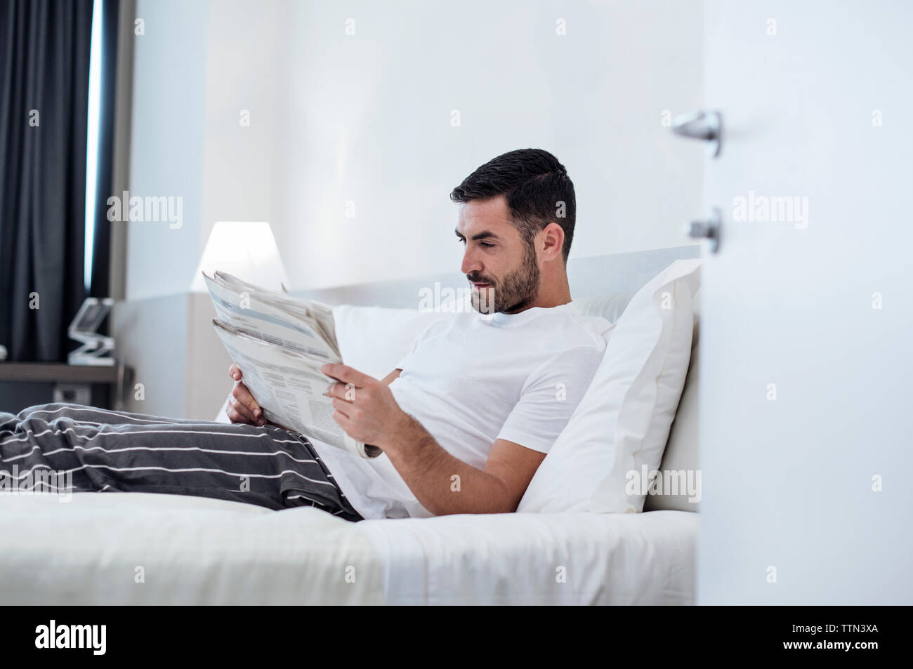 Uomo che legge il giornale mentre vi rilassate sul letto in camera di albergo Foto Stock