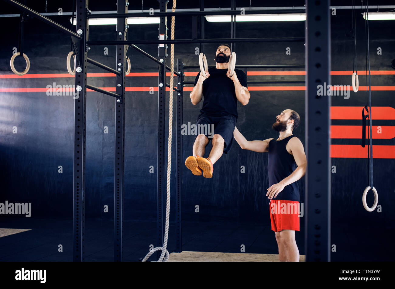 Il Trainer assiste atleta in esercizio su anelli di ginnastica Foto Stock