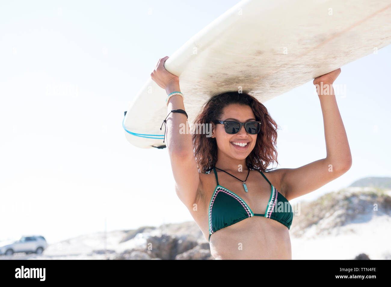 Donna felice che trasportano le tavole da surf sulla testa contro il cielo chiaro durante la giornata di sole Foto Stock