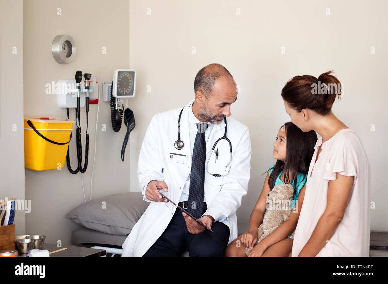 La madre e il medico guardando la figlia mentre è seduto in medical sala esame Foto Stock