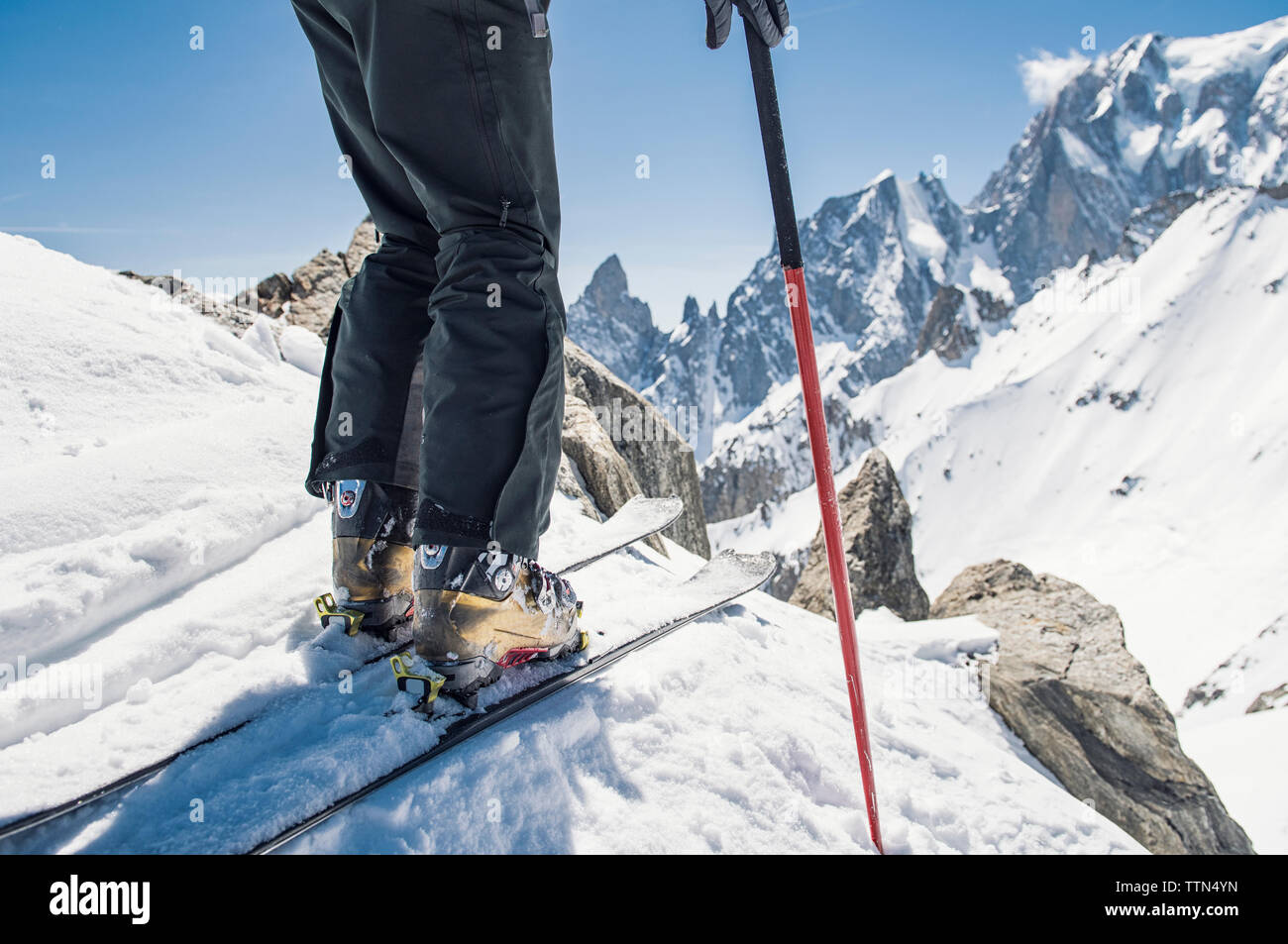 Sezione bassa di un escursionista con gli sci in piedi sulla coperta di neve montagna contro durante la giornata di sole Foto Stock