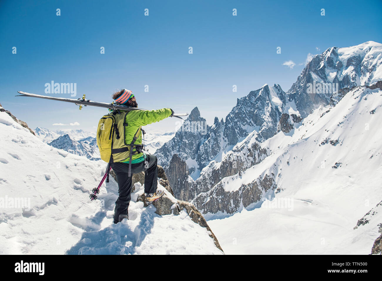 Vista laterale di un escursionista con gli sci in piedi sulla coperta di neve montagna contro il cielo blu chiaro Foto Stock