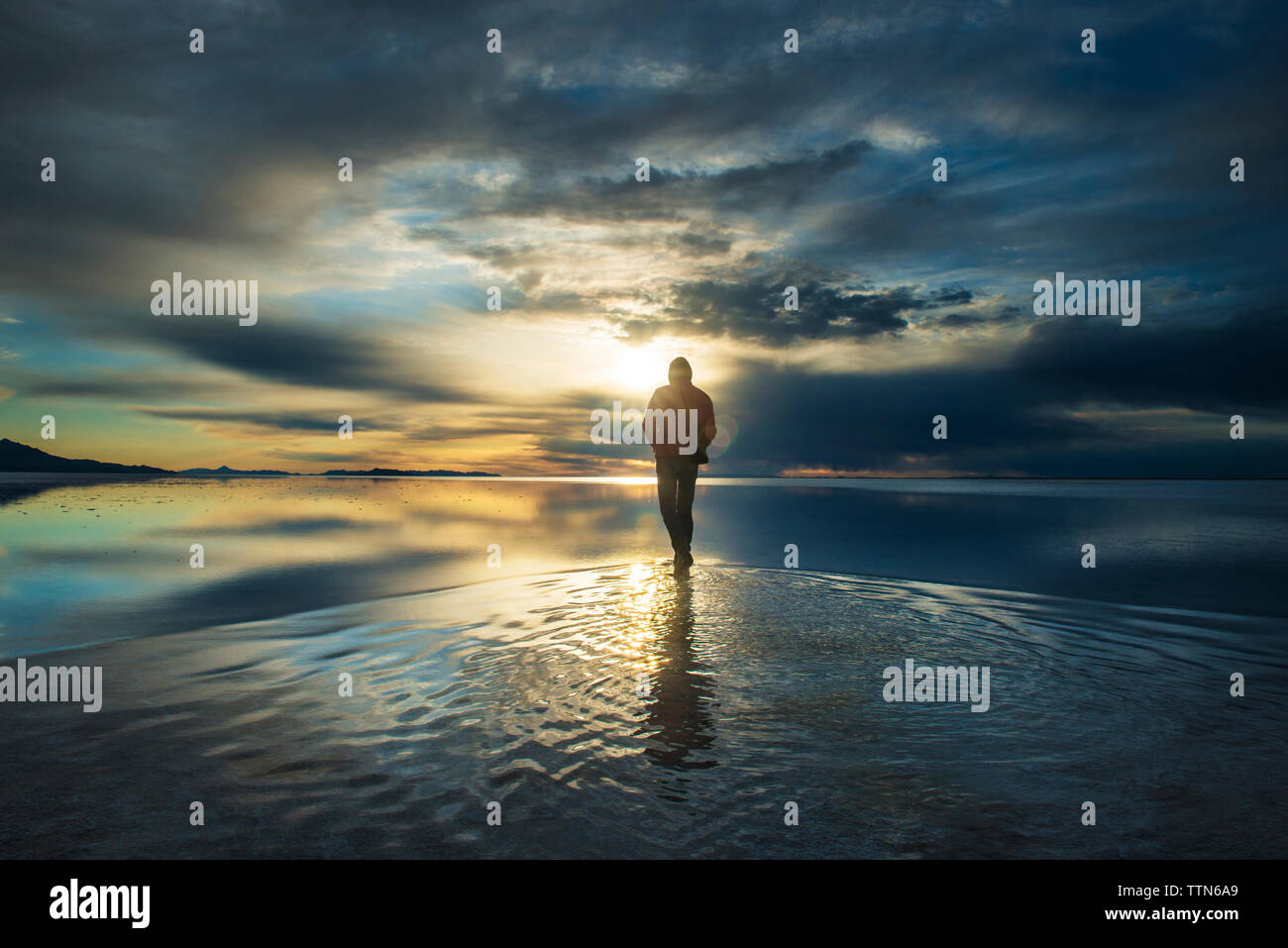 Lunghezza completa di uomo in piedi sulla distesa di sale contro il cielo nuvoloso durante il tramonto Foto Stock