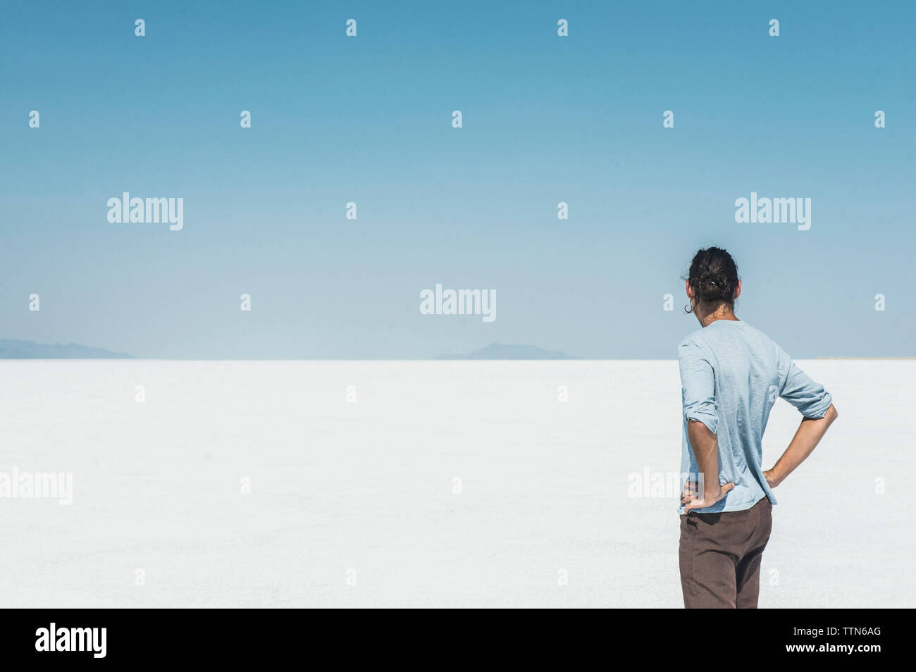 Vista posteriore di uomo in piedi alla distesa di sale contro il cielo blu chiaro Foto Stock