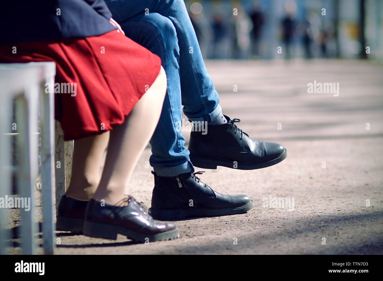 Le gambe di una giovane coppia seduta su un giorno di estate su un banco di  lavoro. L'uomo è vestito in jeans stretti e stivali neri e la donna in un  mantello