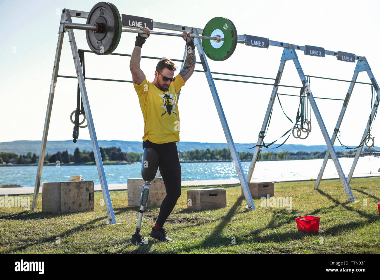 Adattativo maschio atleta deadlift sollevamento stando in piedi contro il lago presso il Park durante la giornata di sole Foto Stock