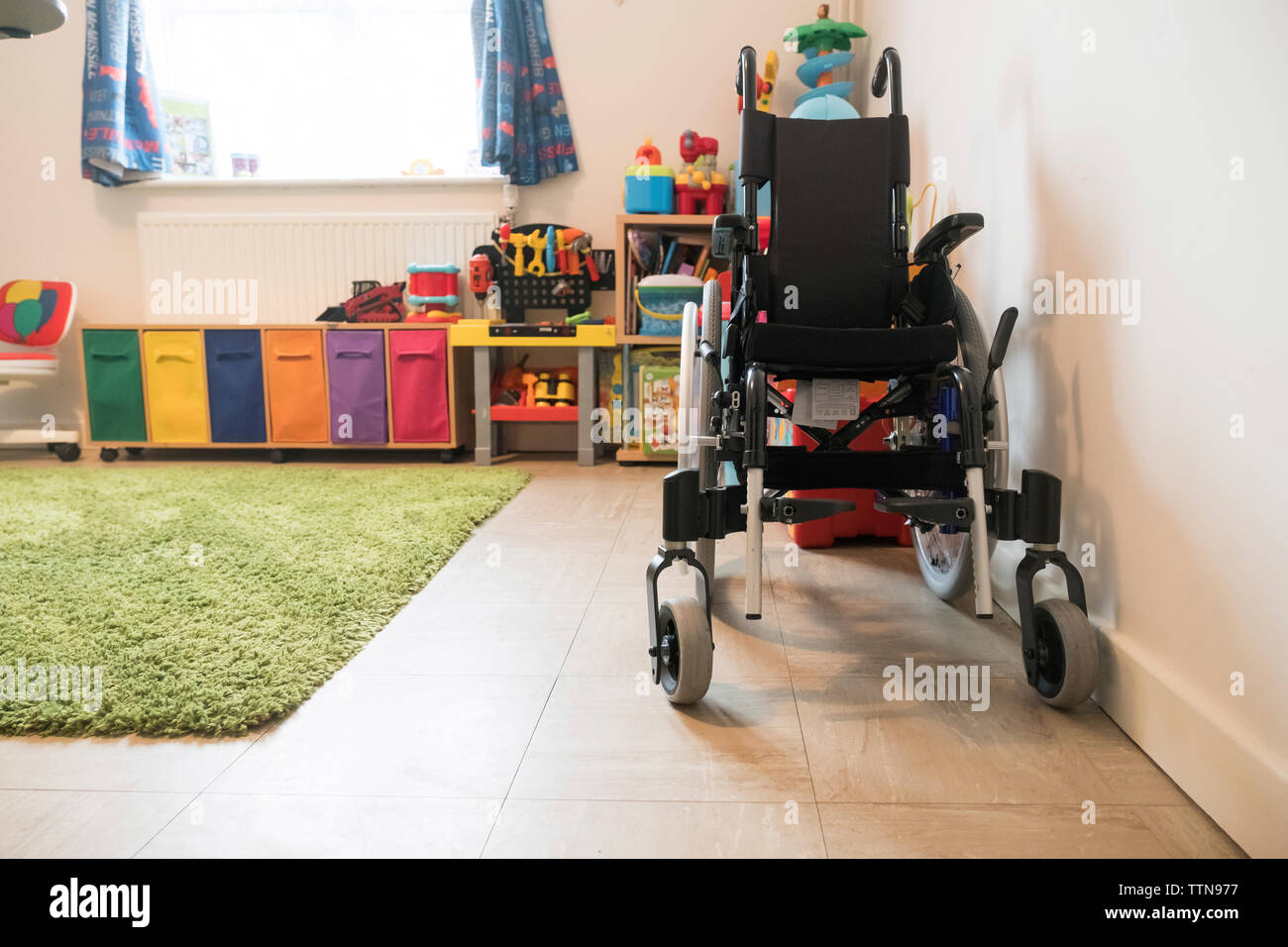 Sedia a rotelle vuota e giocattoli colorati disposti a casa Foto Stock