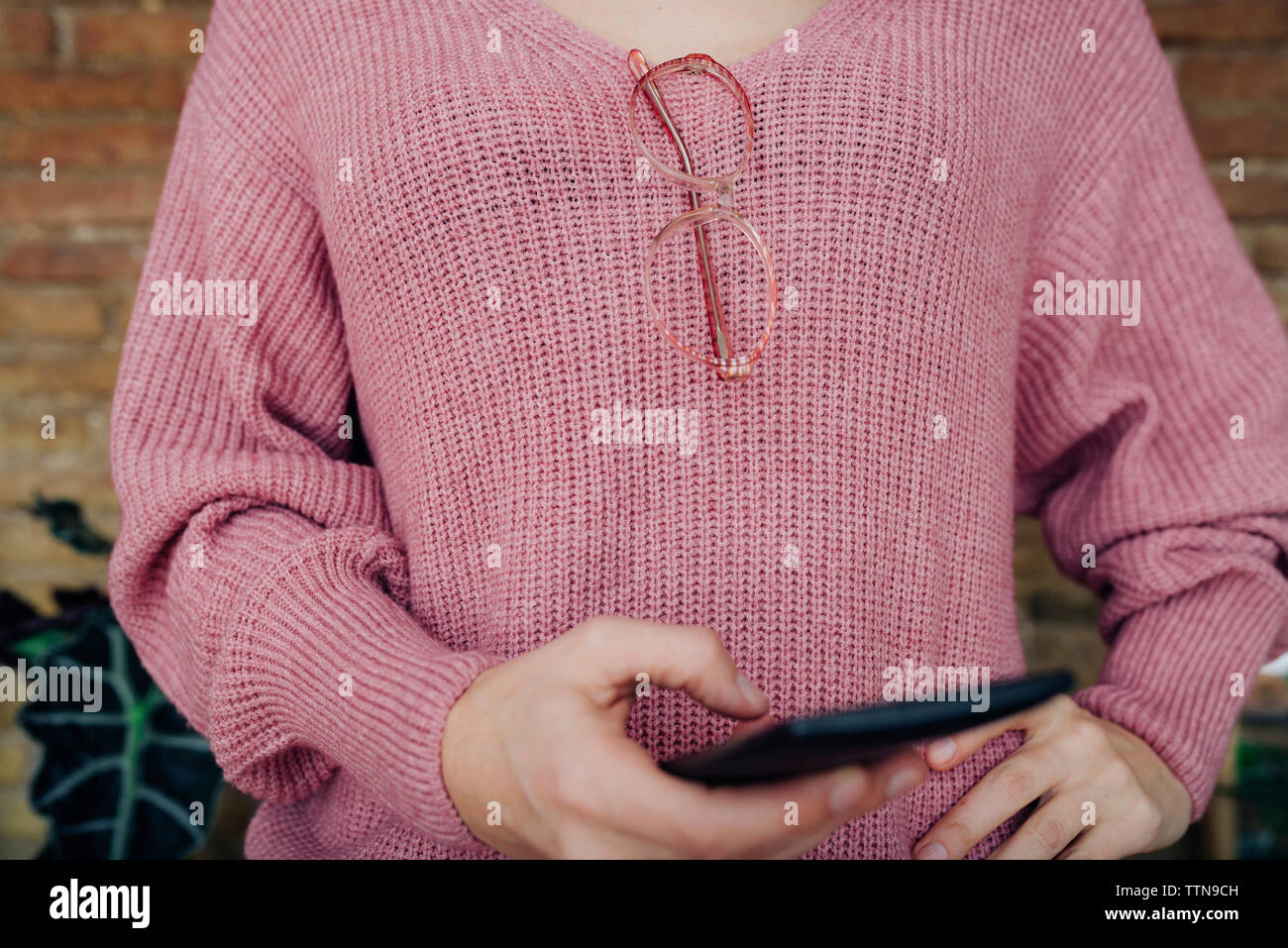Sezione mediana della donna che indossa un maglione mentre utilizzando smart phone Foto Stock