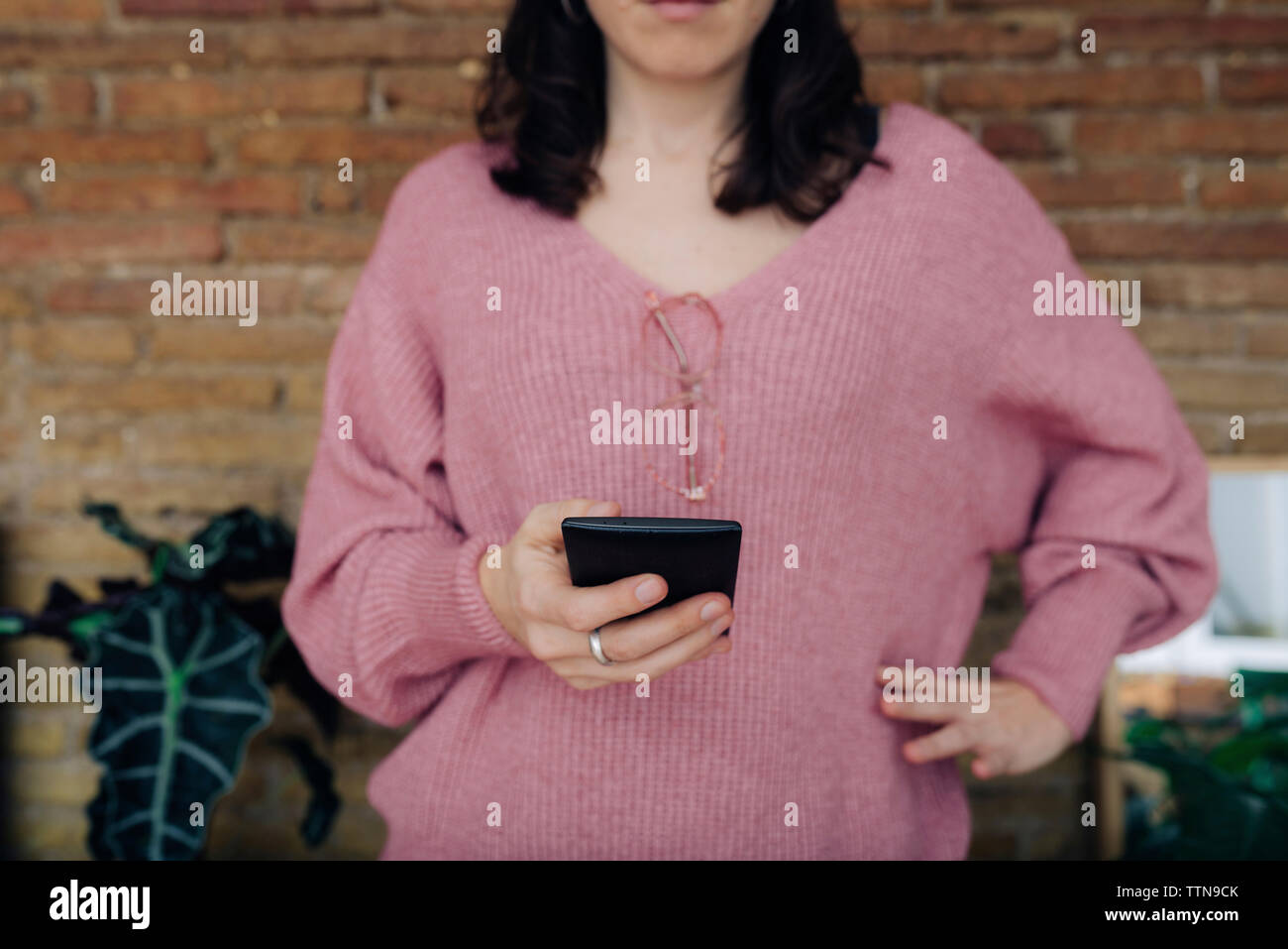 Sezione mediana della donna che indossa un maglione mentre utilizzando smart phone a casa Foto Stock