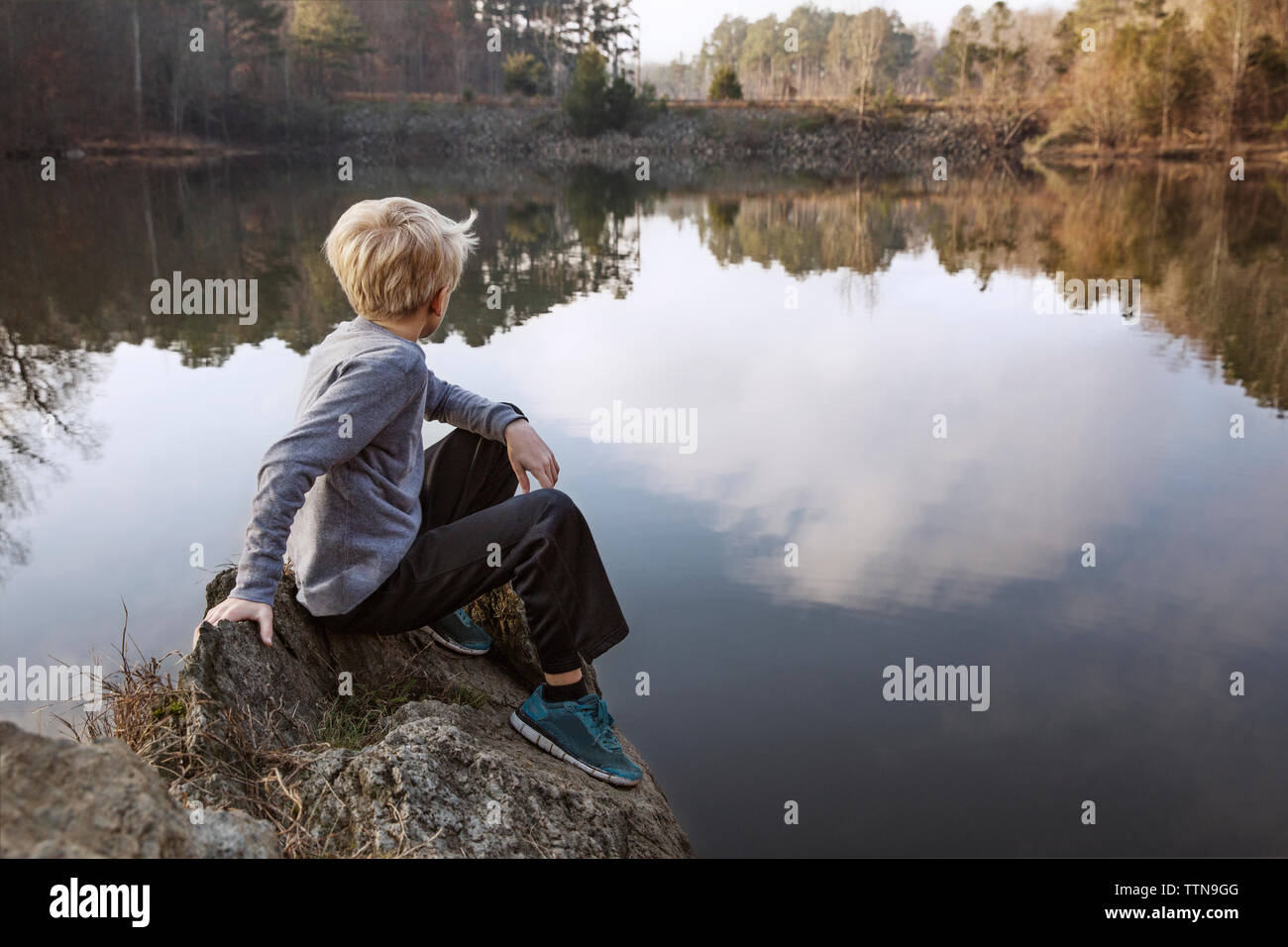 Ragazzo seduto sulla roccia dal lago Foto Stock