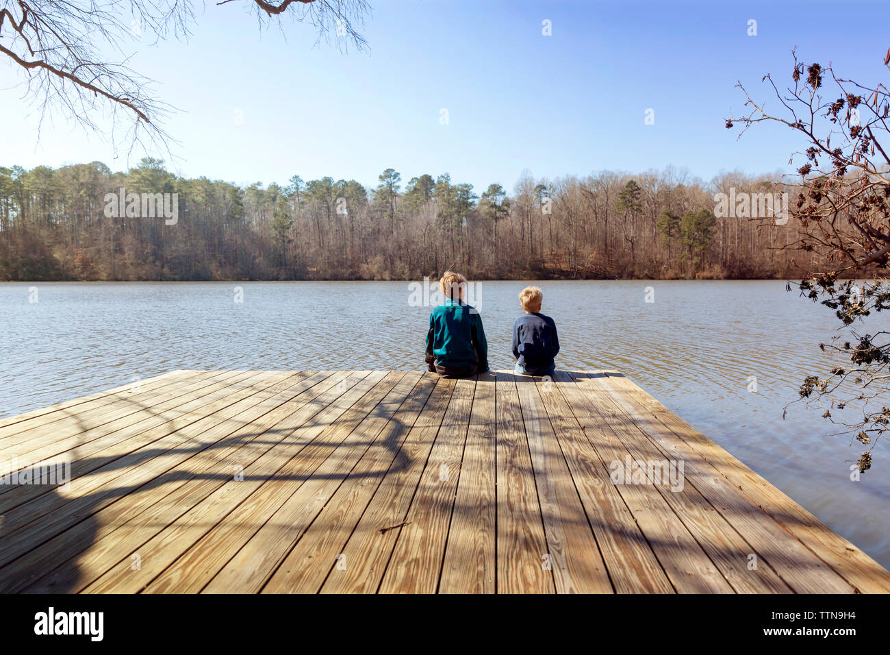 Vista posteriore dei ragazzi seduta sul bordo del molo sul lago Foto Stock