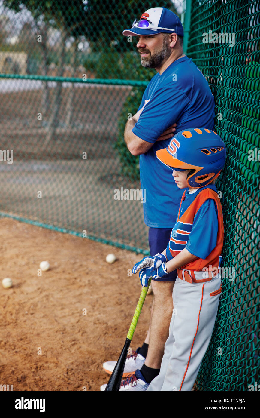 Vista laterale di pensosa giocatore di baseball e coach in piedi da opaco recinto sul campo Foto Stock