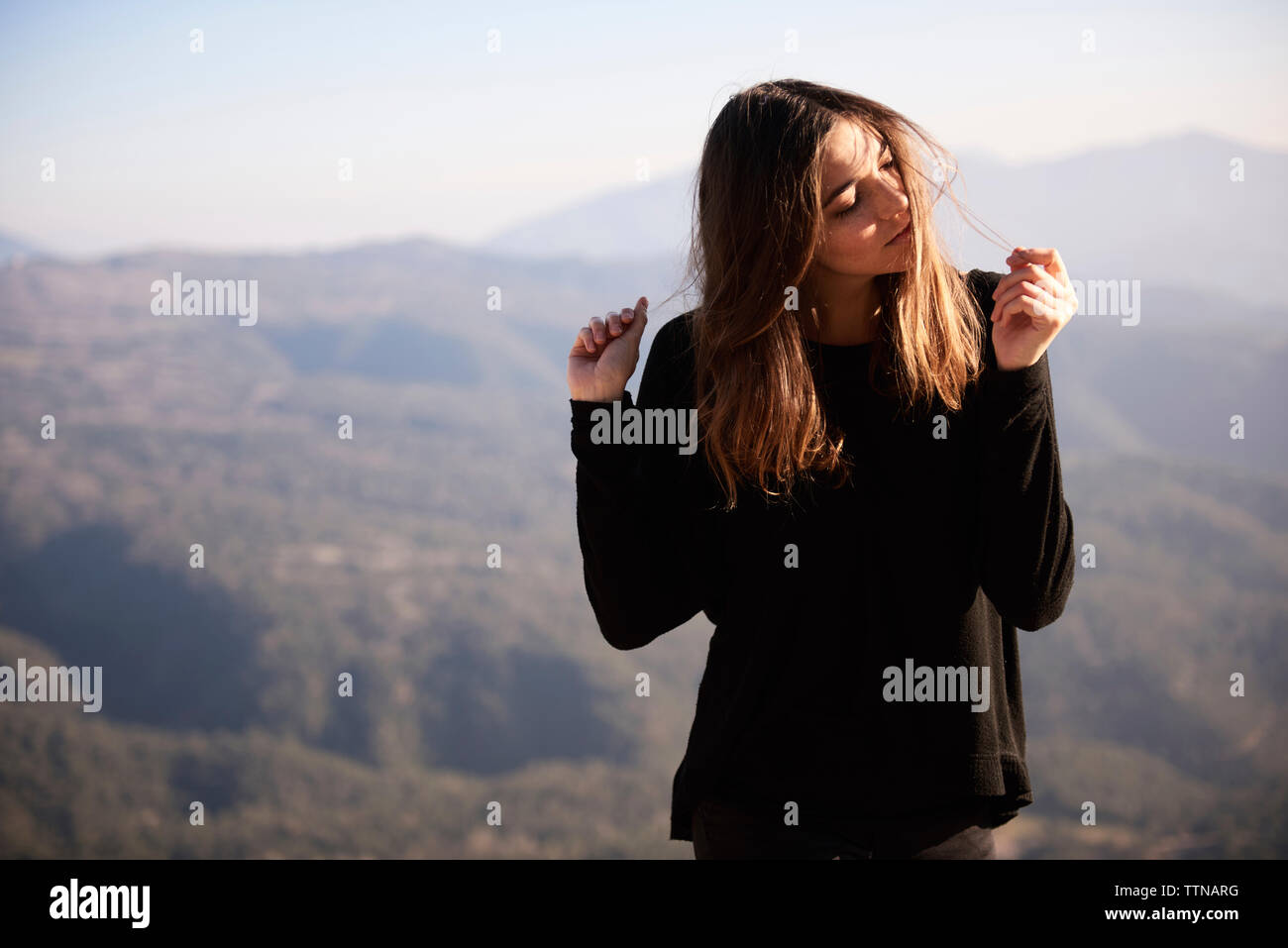 Donna che gioca con i capelli mentre in piedi contro le montagne Foto Stock