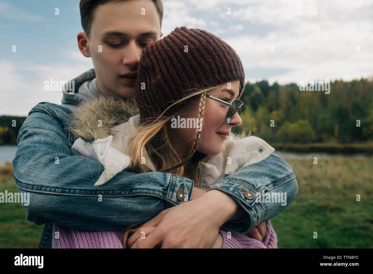 Fidanzato abbracciando la fidanzata mentre in piedi contro il cielo nuvoloso in foresta Foto Stock
