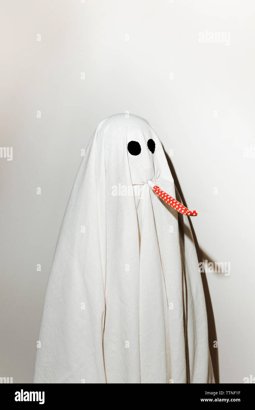 Uomo in costume fantasma soffiando parte ventilatore avvisatore acustico mentre in piedi contro la parete Foto Stock