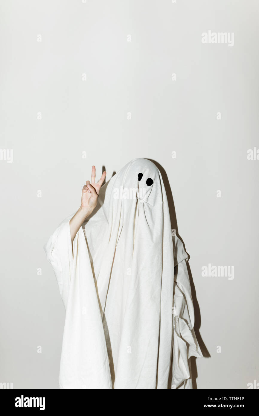 Uomo in costume fantasma che mostra segni di pace mentre in piedi contro la parete Foto Stock