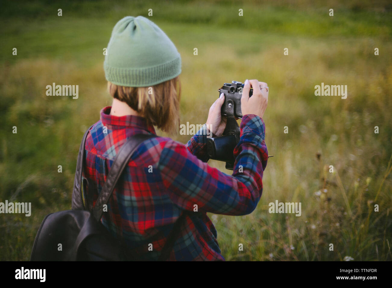 Vista laterale della donna con zaino fotografare mentre si sta in piedi sul campo erboso Foto Stock