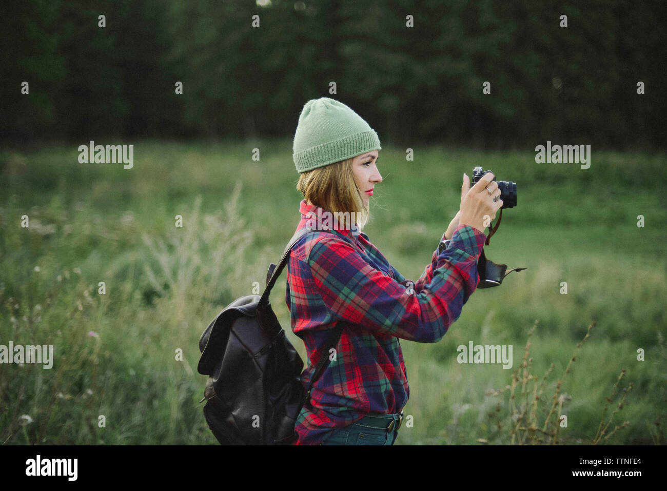 Donna con zaino fotografare mentre si sta in piedi sul campo erboso Foto Stock