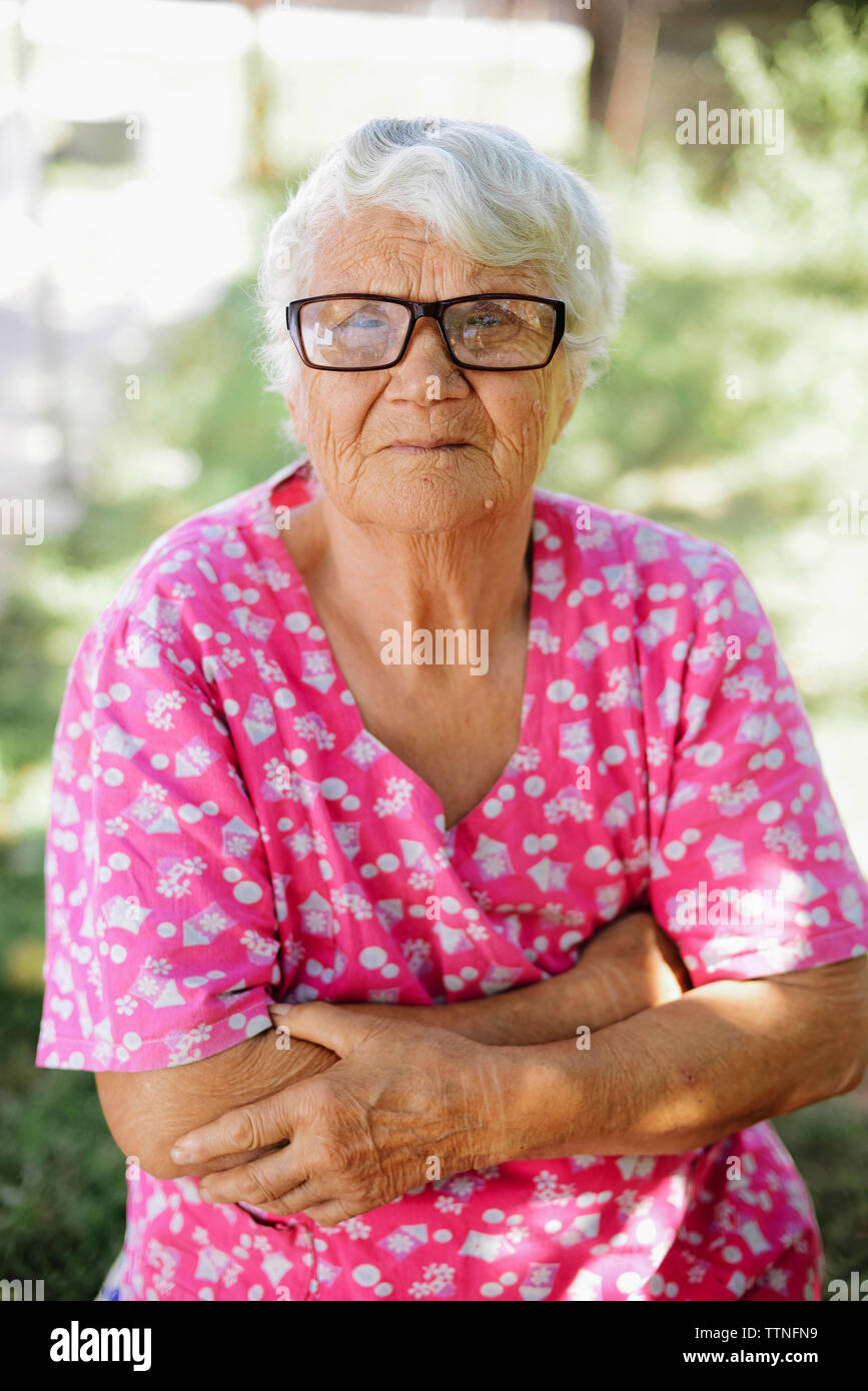Ritratto di donna senior con le braccia incrociate indossando occhiali a backyard Foto Stock