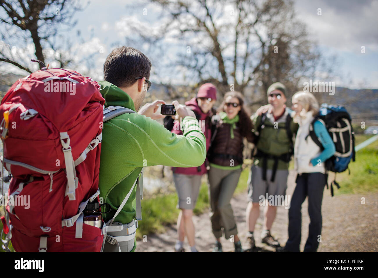 Escursionista maschio a fotografare gli amici in piedi sul campo tramite la fotocamera Foto Stock