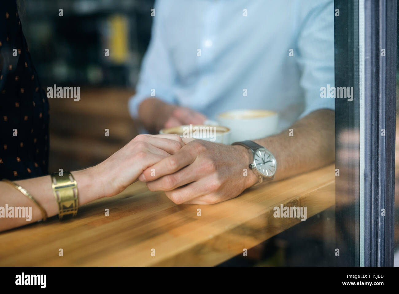 Giovane tenendo le mani sul tavolo visto attraverso la finestra al cafe Foto Stock Giovane tenendo le mani sul tavolo visto attraverso la finestra al cafe Foto Stock